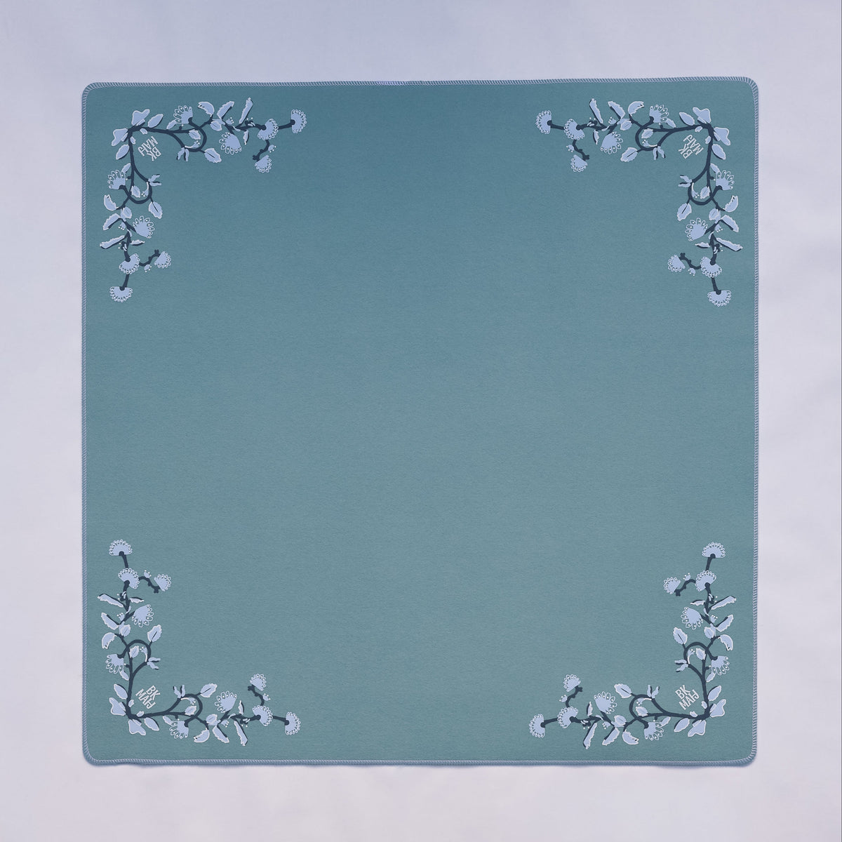 A light blue colored felt mahjong mat with delicate floral designs in each corner.