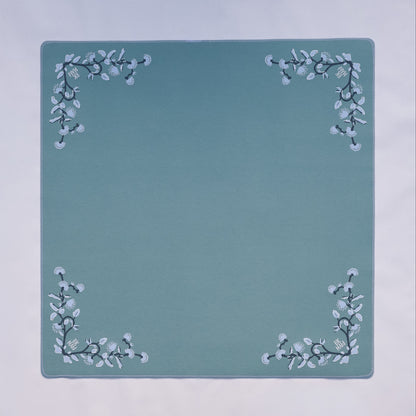 A light blue colored felt mahjong mat with delicate floral designs in each corner.